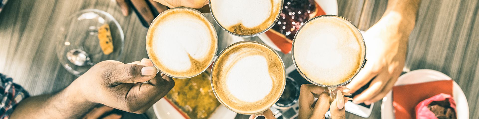 Friends clink coffee mugs over a shared meal, toasting a cozy moment together.