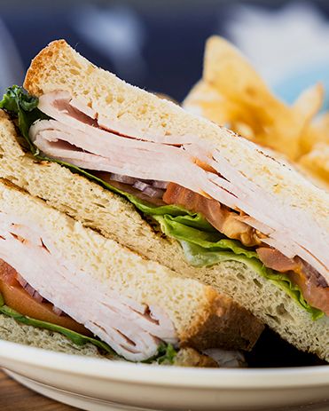 A turkey club sandwich: stacked toast with turkey, lettuce, tomato, and mayo, served with potato chips on the side.